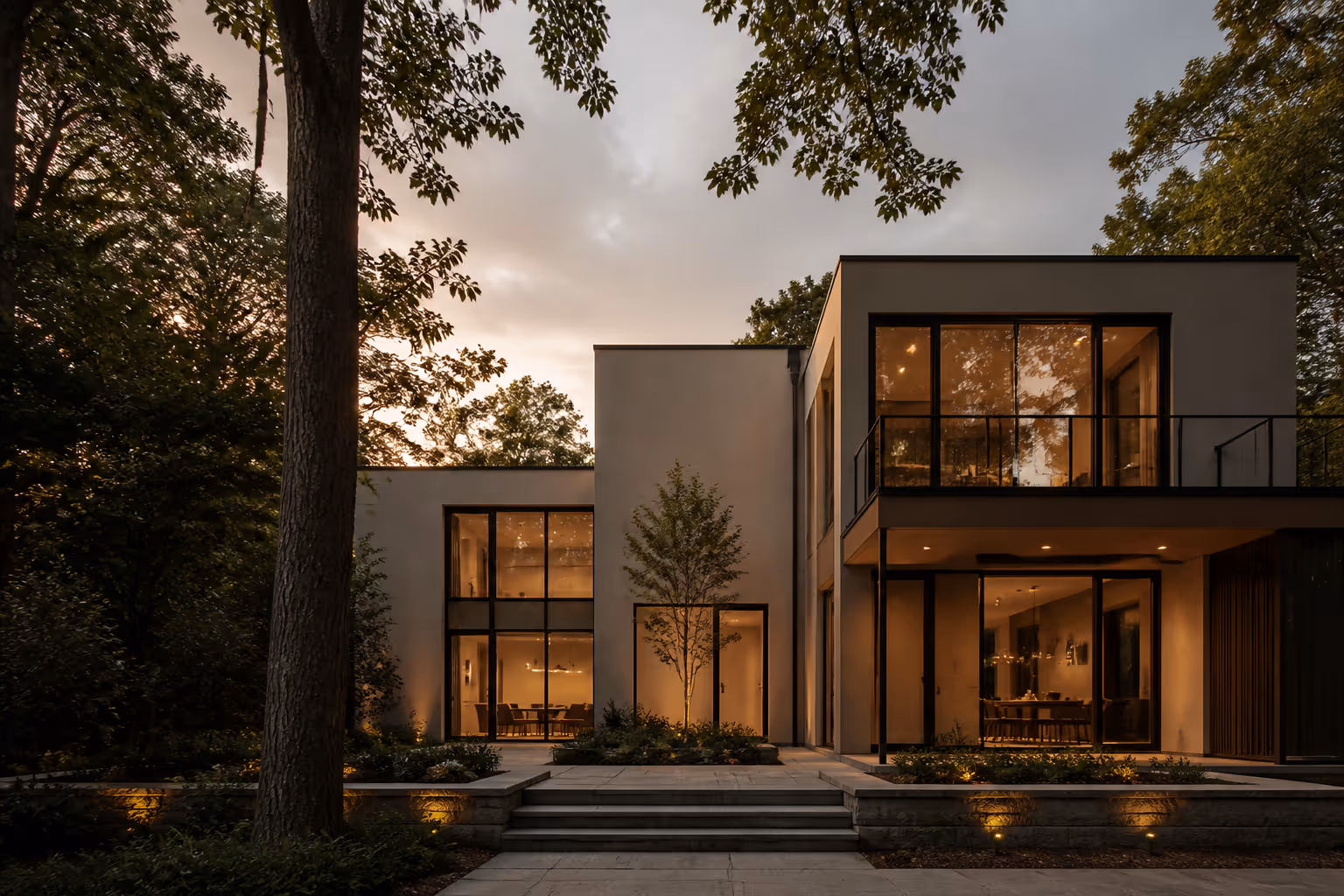 Contemporary house facade nestled among pine trees at dusk with warm interior glow